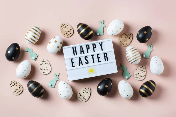 Happy Easter frame with golden, white, black dotted and striped eggs on a pink background. Top view, flat lay. Modern Easter greeting card