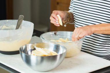 Woman putting apples while cooking apple pie in the modern kitchen