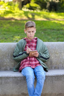 Deftere yazan yakışıklı bir genç şehir sokaklarında bir bankta oturuyor, açık havada. Kafkas delikanlısı arkadaşlarını yürüyüş için bekliyor. 