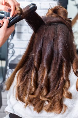 Modern bir kuaförde müşterilerin saçlarını kıvırmak için ütü kullanan profesyonel bir kuaför. Kuaför, saçını kestirirken beyaz kadın için özel muamele uyguluyor.