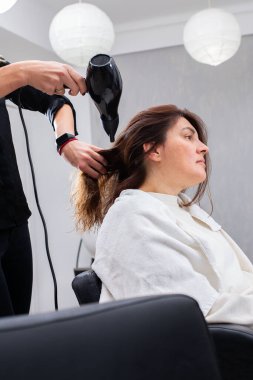 Modern bir kuaförde profesyonel kuaför müşterilerin saçlarını bir pervaneyle kurutuyor. Kuaför, saçını kestirirken beyaz kadın için özel muamele uyguluyor.