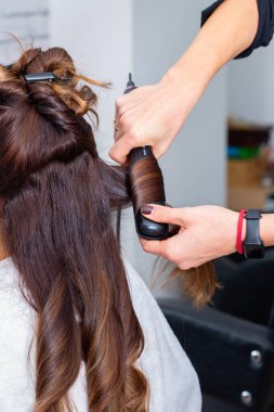 Modern bir kuaförde müşterilerin saçlarını düzleştirmek için saç maşası kullanan profesyonel bir kuaför. Kuaför, saçını kestirirken beyaz kadın için özel muamele uyguluyor.