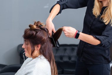 Modern bir kuaförde müşterilerin saçlarını düzleştirmek için saç maşası kullanan profesyonel bir kuaför. Kuaför, saçını kestirirken beyaz kadın için özel muamele uyguluyor.