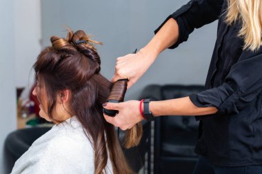 Modern bir kuaförde müşterilerin saçlarını düzleştirmek için saç maşası kullanan profesyonel bir kuaför. Kuaför, saçını kestirirken beyaz kadın için özel muamele uyguluyor.