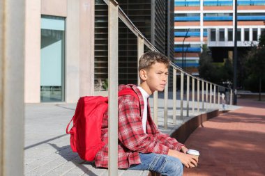 Yakışıklı genç, şehir sokaklarında dinlenmek için kahve içiyor. Kafkasyalı genç dışarıda yürüyor. 