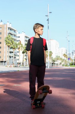 Dışarıda kaykayla duran yakışıklı bir genç. Gençler sokaklarda dolaşıp şehri keşfediyorlar.