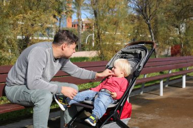 Baba ve oğul bankta oturup şehir parkında oynuyorlar. 