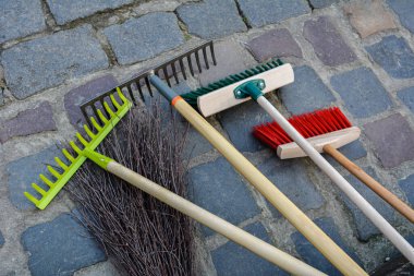 Şehir caddesini temizlemek için ekipman. Parkın çitlerinin yanında tırmık, kürek, süpürge tezgahı. Çimleri enkazdan temizlemek için hafif tırmık ve sert plastik süpürge yardımcıları..