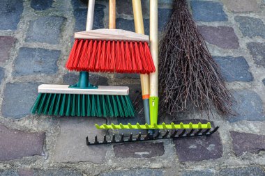 Şehir caddesini temizlemek için ekipman. Parkın çitlerinin yanında tırmık, kürek, süpürge tezgahı. Çimleri enkazdan temizlemek için hafif tırmık ve sert plastik süpürge yardımcıları..