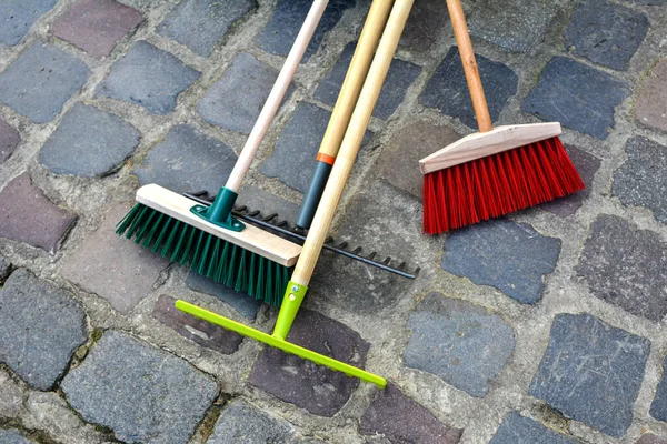 城市街道的清洁设备 扫帚站在公园栅栏旁边 轻便耙和硬塑料扫帚帮助清理草坪上的瓦砾 — 图库照片