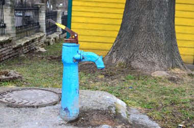 Sonbaharda eski paslı su sütunu, seçici odak, bulanık arkaplan. Köy sokaklarının arka planına karşı SSCB döneminin eski usul su musluğu..