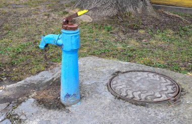 Sonbaharda eski paslı su sütunu, seçici odak, bulanık arkaplan. Köy sokaklarının arka planına karşı SSCB döneminin eski usul su musluğu..