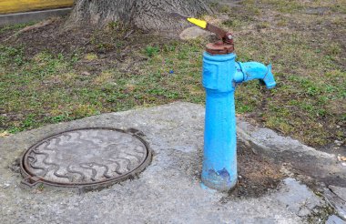 Sonbaharda eski paslı su sütunu, seçici odak, bulanık arkaplan. Köy sokaklarının arka planına karşı SSCB döneminin eski usul su musluğu..