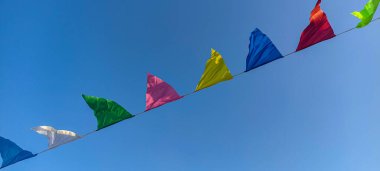 Mavi gökyüzünün önündeki renkli bayrakların çizgileri. Küçük renkli bayraklar. Mavi gökyüzüne karşı renkli üçgen bayraklar. .