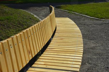 View of a long wooden bench and a green lawn in the city square . Arrangement of the park comfortable places for recreation, a large wooden bench in the park in the city center.
