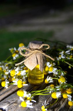Eski ahşap arka planda Roma papatyası yağı bulunan küçük cam şişe. Papatya çiçekleri, yaklaşın. Aromaterapi, spa ve bitkisel ilaç malzemeleri. Boşluğu kopyala.