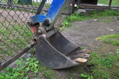 Mini kazıcı kovasını kapatıyoruz. Bahçe alanında toprağı kazıyoruz. Mini kazıcı. Mini kazıcı park etmiş, kazı işi dışarıda..