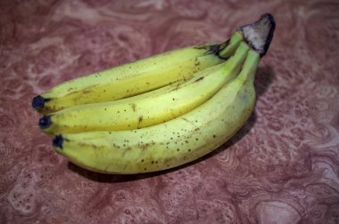 Masanın üzerinde taze muzlardan bir dal, yakın plan. Masanın üzerinde satılmaya hazır yeşil ve sarı gölgeli bir muz yığını..