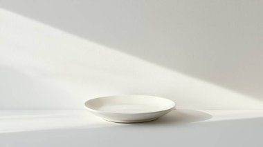 Temiz bir yüzeyde duran beyaz bir plaka içeren minimalist bir tasarım. Yumuşak ışık yumuşak gölgeler yaratır, kompozisyonun basit zarafetini arttırır. Yemek sanatı ya da iç dekorasyon için mükemmel..