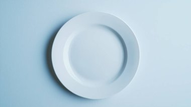 Yumuşak mavi arka plana yerleştirilmiş minimalist beyaz bir plaka. Bu resim yemek temaları ve sanatsal sunumlar için ideal basitlik ve zarafeti yakalar.