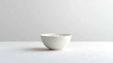 İnce bir dokuya sahip minimalist bir beyaz kase pürüzsüz bir ışık yüzeyine dayanır. Tasarımda sadelik ve zarafet arayanlar için mükemmel, herhangi bir ayarı geliştirmek için.