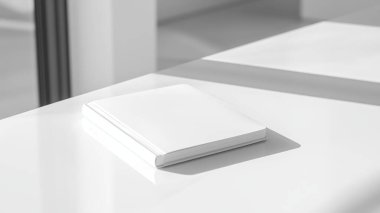 Boş beyaz bir kitap minimalist bir yüzeye dayanır, yumuşak gölgeler bırakır. Temiz tasarım ve parlak atmosfer okuma ve yazma için davet edici bir alan yaratır..
