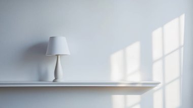 Minimalist bir iç mekan beyaz bir rafta şık bir masa lambası sergiliyor. Yumuşak gölgeler ve temiz çizgilerle sakin bir atmosfer yaratıyor..