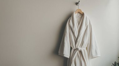 A cozy white bathrobe elegantly hanging on a wall, perfect for enhancing a minimalist bathroom aesthetic. Ideal for promoting relaxation and comfort. clipart