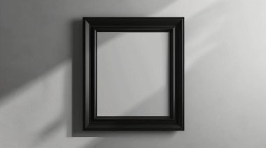 Boş bir siyah fotoğraf çerçevesi gri bir duvara dayanıyor, yumuşak gölgeli minimalist bir tasarım sergileniyor, sanat gösterileri veya yaratıcı sunumlar için ideal..