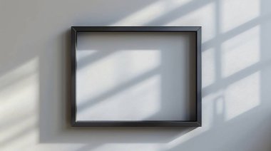 Duvara dayalı boş siyah bir çerçeve, yumuşak doğal ışıkla aydınlatılmış büyüleyici gölgeler yaratarak, minimalist ve zarif bir atmosfer yaratıyor..