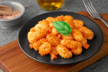 Close-up of a black plate of POTATO GNOCCHI in tomato sauce and a basil leaf on a cutting board. Studio shot.