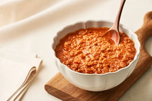 A bowl of fresh BOLOGNESE SAUCE on a wooden cutting board on a linen tablecloth. Studio shot. Close-up from a high angle.