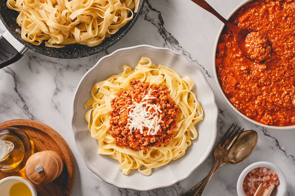 Plate of fresh tagliatelle pasta with bolognese sauce and bowl of fresh BOLOGNESE SAUCE and a pan of cooked tagliatelle pasta. Top view.