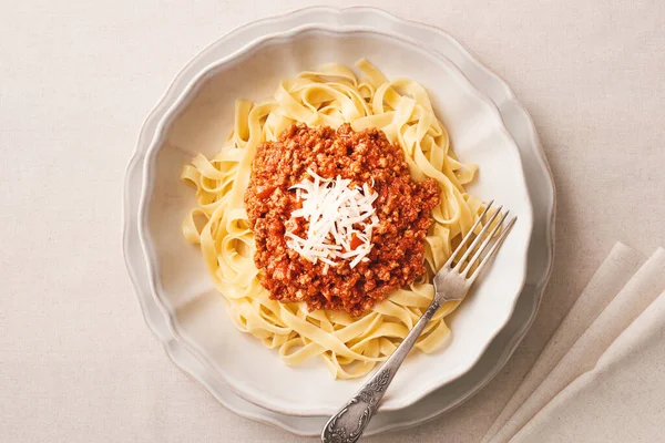 Plate of fresh tagliatelle pasta with bolognese sauce linen beige tablecloth. Top view. One object.