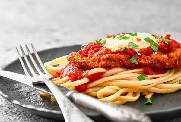 Close-up of a plate of homemade Chicken Parmesan with spaghetti on a gray stone background.