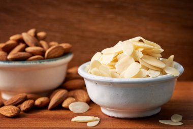 Küçük bir kase gevrek badem ve bir kase tam badem. Düşük açıyla yakın çekim.