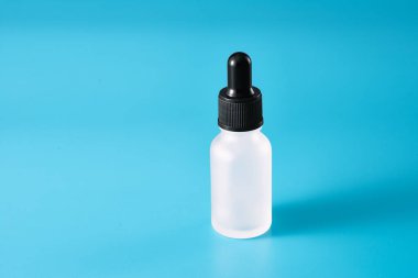 İçinde kozmetik ürünler olan bir pipetin olduğu cam bir şişe. Mavi arka plan. Boşluğu kopyala.