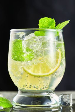 Gri arka planda mojito kokteyli olan bir bardağa yakın plan. Düşük açıyla dikey çekim.