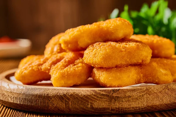 stock image Close-up of fried golden-colored nuggets in a wooden plate. Studio shot from a low angle.