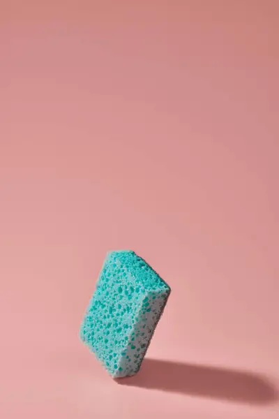 Kitchen sponge for cleaning green color on a pink background with copy space. Single object. Vertical frame. Studio shot.