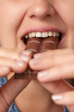 Çikolata ısıran mutlu, beyaz bir kadının ağzını kapat. Ön manzara. Dikey çerçeve. Düşük açı görünümü.