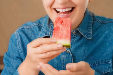 Gülümseyen beyaz bir kadın tarafından ağzına getirilen taze bir karpuz parçasının yakın çekimi. Ön manzara. Düşük açı görünümü.