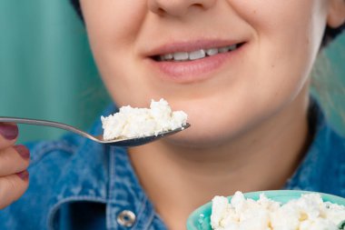 Elinde bir kase süzme peynir ve kaşıkla gülümseyen beyaz bir kadının yakın çekimi. Ön üç çeyrek görüntü. Düşük açı. Kapalı.