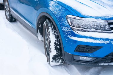 Karla kaplı bir yolda duran mavi ve modern bir arabanın önü dörtte üçlük bir manzara..