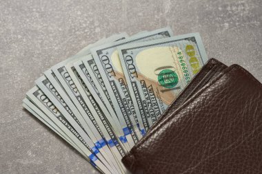 Kahverengi bir cüzdan ve yığınla yüz dolarlık banknot. Üst görünüm.