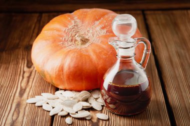 Bir şişe balkabağı yağı, balkabağı meyvesi ve ahşap arka planda kurumuş tohumlar..