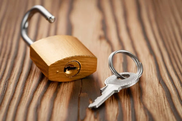 Close-up of a key and an unlocked padlock in golden color on a wooden background. Low angle view.