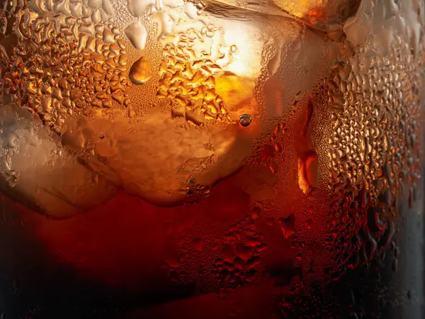 Droplets on the wall of a glass of cola with ice cubes. Macro shot.