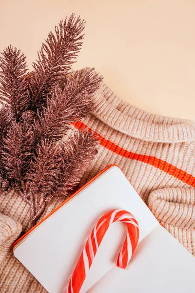 居心地の良いセーターでクリスマスフラットレイ ローズゴールド松の木の枝 キャンディー杖とメモ帳ベージュの背景に隔離された 新年のコンセプト ストック画像