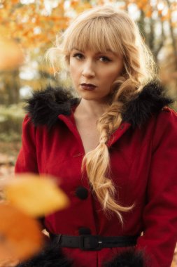 Sonbahar yaprakları içindeki kadın kırmızı ceket giyiyor.